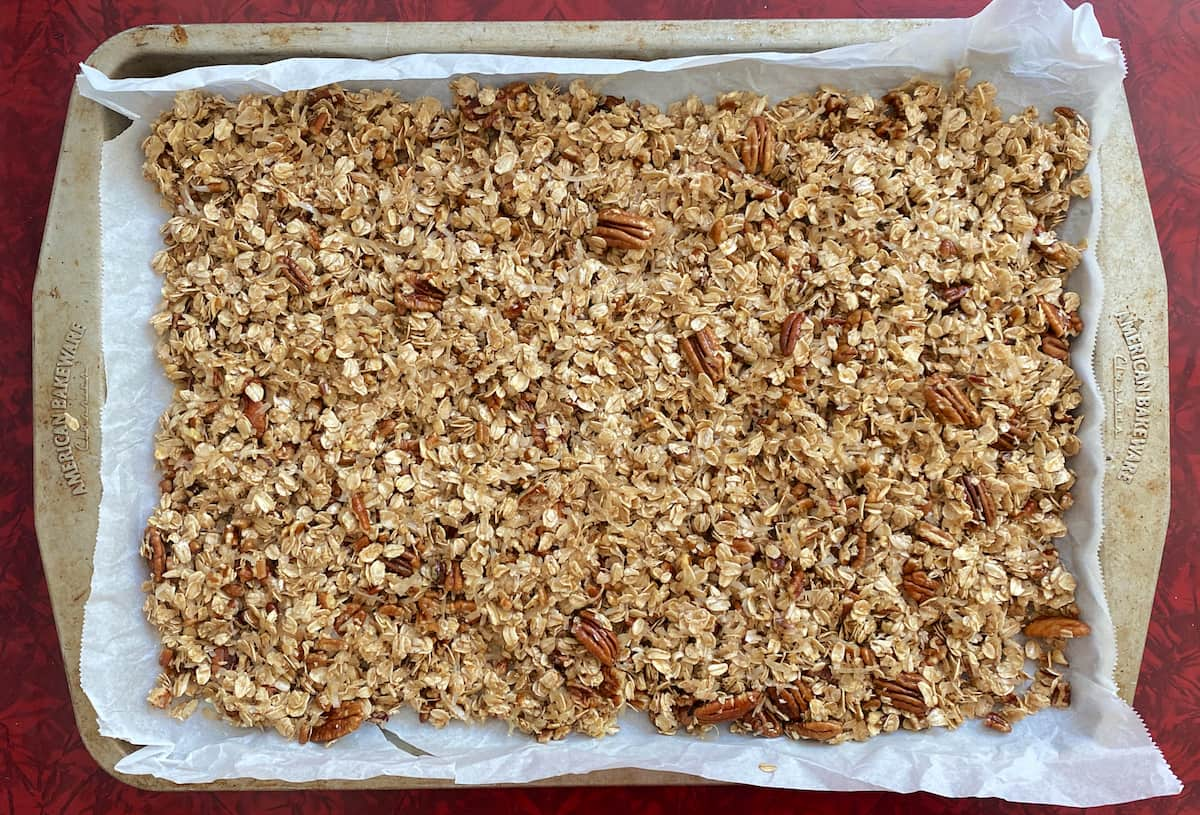 Granola, fully baked, on a parchment covered baking sheet.