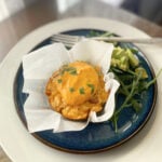 Breakfast casserole muffin on a plate with arugula and chopped avocado.