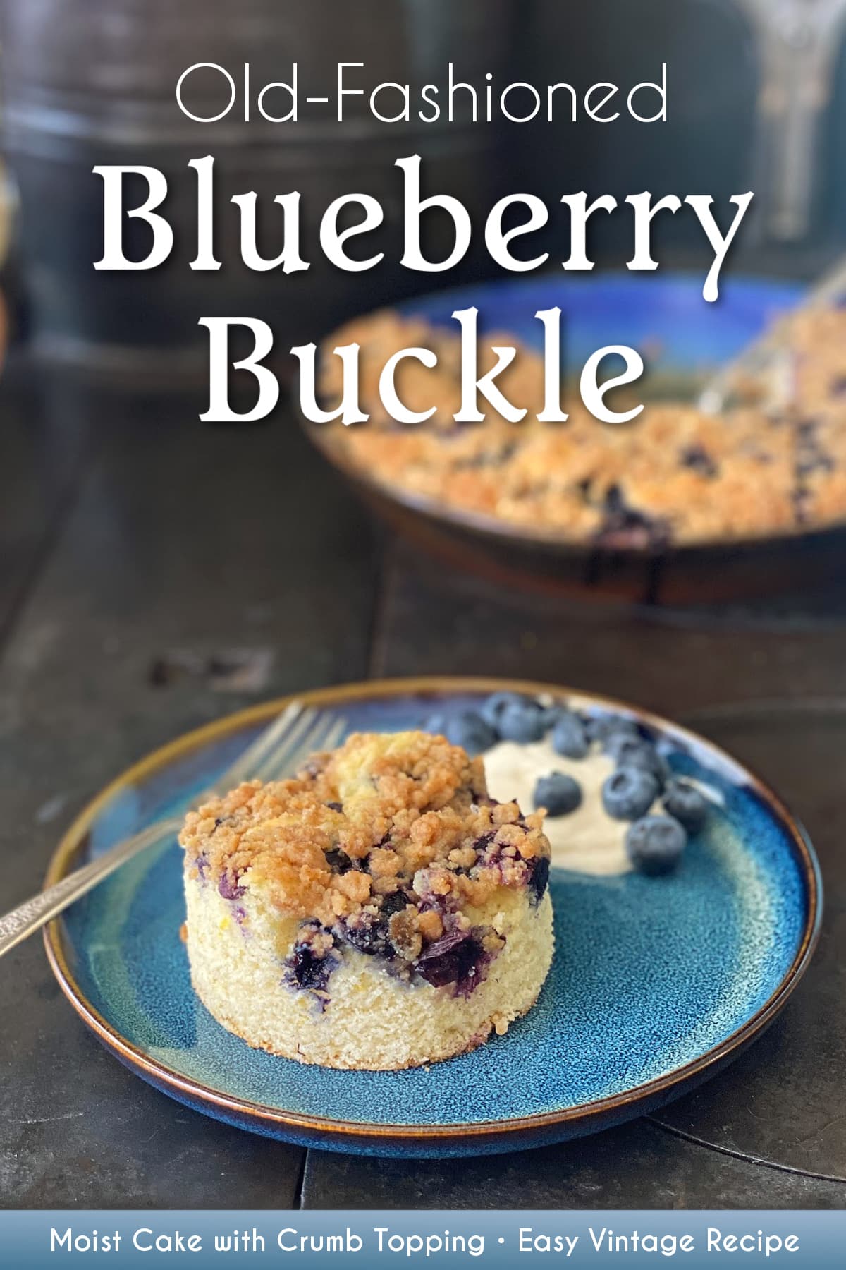 A round-cut piece of blueberry buckle on a plate, with a dollap of yogurt and a sprinkle of fresh blueberries on the side. The remaining unserved buckle is in the background. Pin text reads "Old fashioned Blueberry Buckle | Moist Cake with Crumble Topping • Easy Vintage Recipe". 