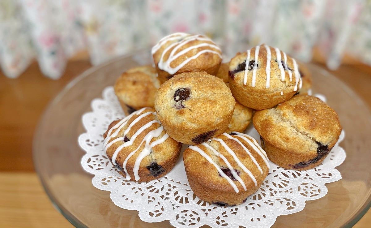 Gluten-free lemon blueberry muffins with and without icing stacked on a cake tray for serving.