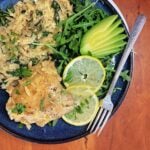 Overhead shot of plated lemon chicken thighs with creamy orzo, garnished with baby arugula, lemon slices, and avocado fan.
