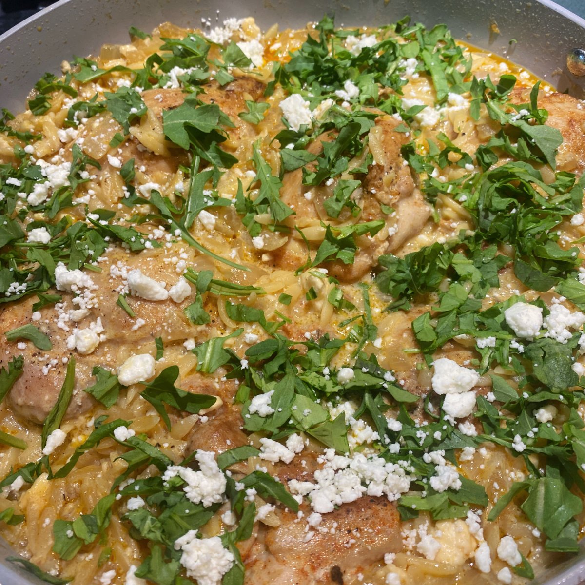 closeup of lemon chicken orzo, fully cooked and garnished with arugula and feta.