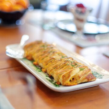 Close-up of a raided puff pastry breakfast roll on a long serving plate, on a nicely set table.