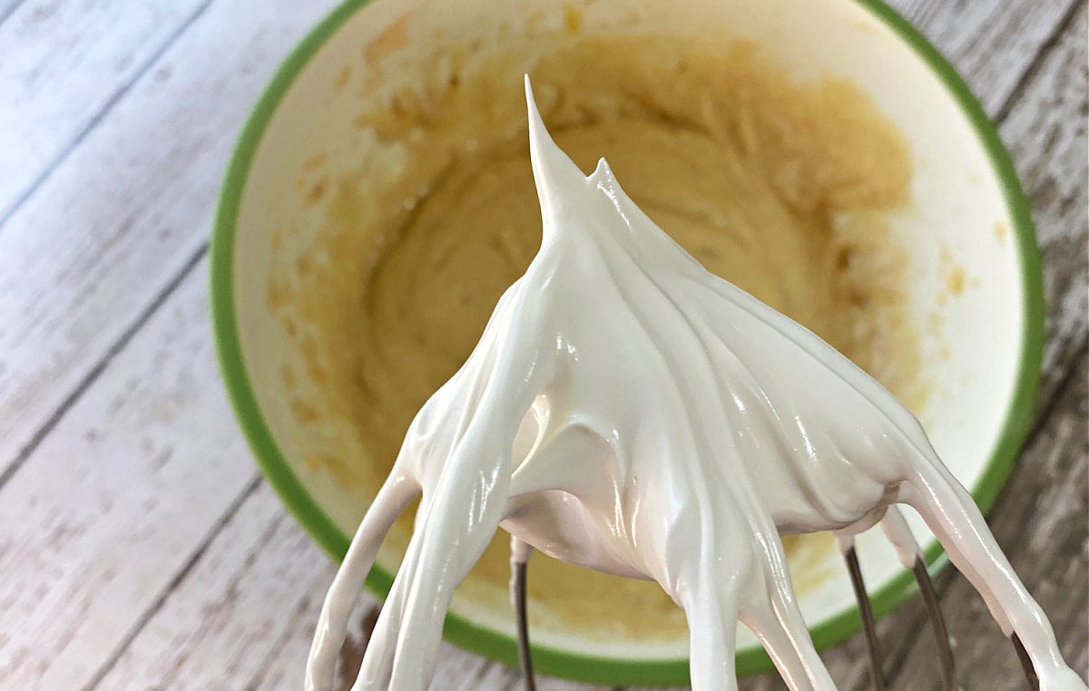 Egg whites being whipped into glossy meringue with stiff peaks.
