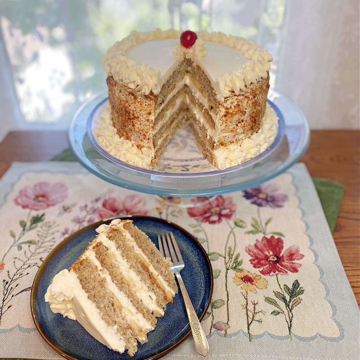 Whole Banana Cream Chiffon Cake on a stand, topped with whipped cream and banana slices. Slice of cake on small plate,  showing fluffy layers, fresh banana slices, and whipped cream frosting.