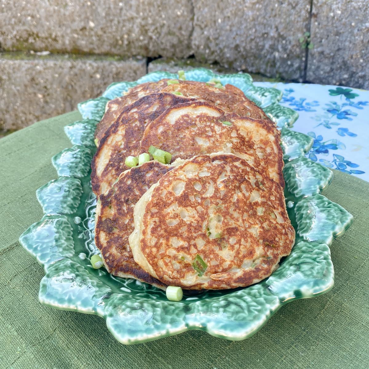 Irish boxty potato pancakes stacked on a plate with crispy golden edges. Garnished with green onions.