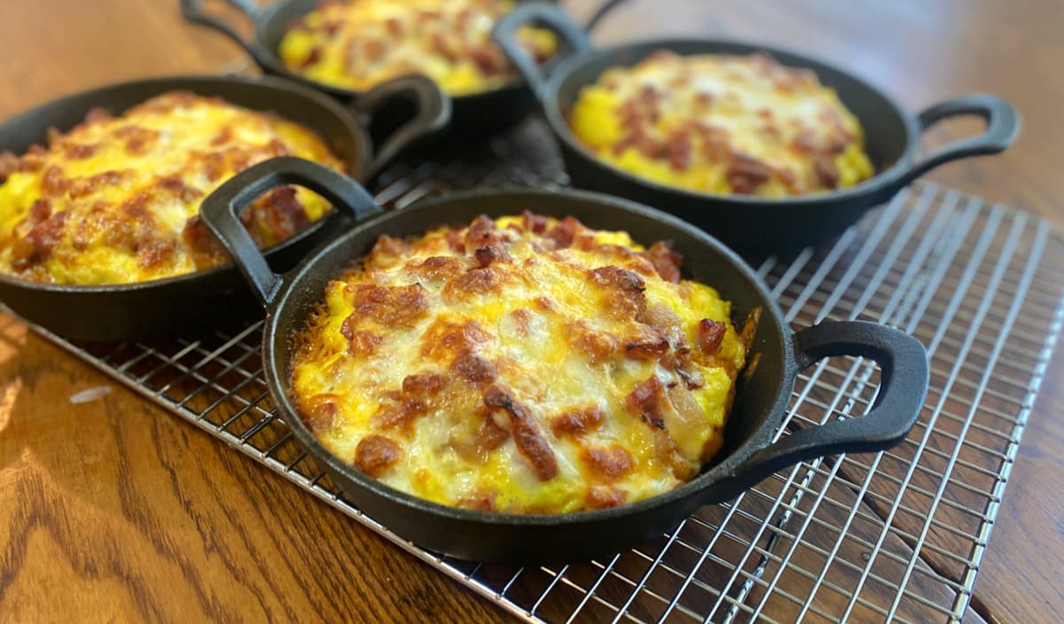 Freshly baked cast iron breakfast pizzas with golden crusts and melted cheese cooling in mini skillets.