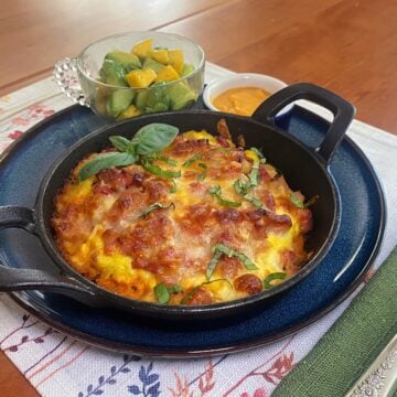 Mini cast iron breakfast pizzas topped with scrambled eggs, melted cheese, bacon, and vegetables, baked until golden and served in individual cast iron skillets.