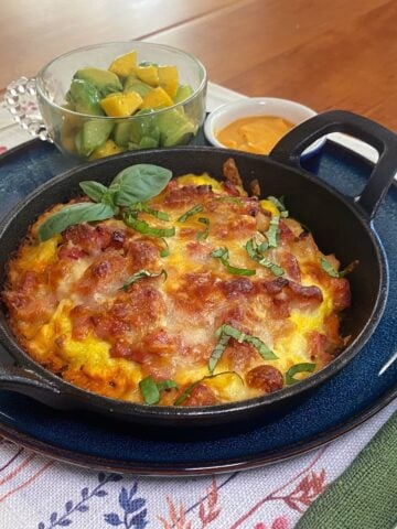 Mini cast iron breakfast pizzas topped with scrambled eggs, melted cheese, bacon, and vegetables, baked until golden and served in individual cast iron skillets.