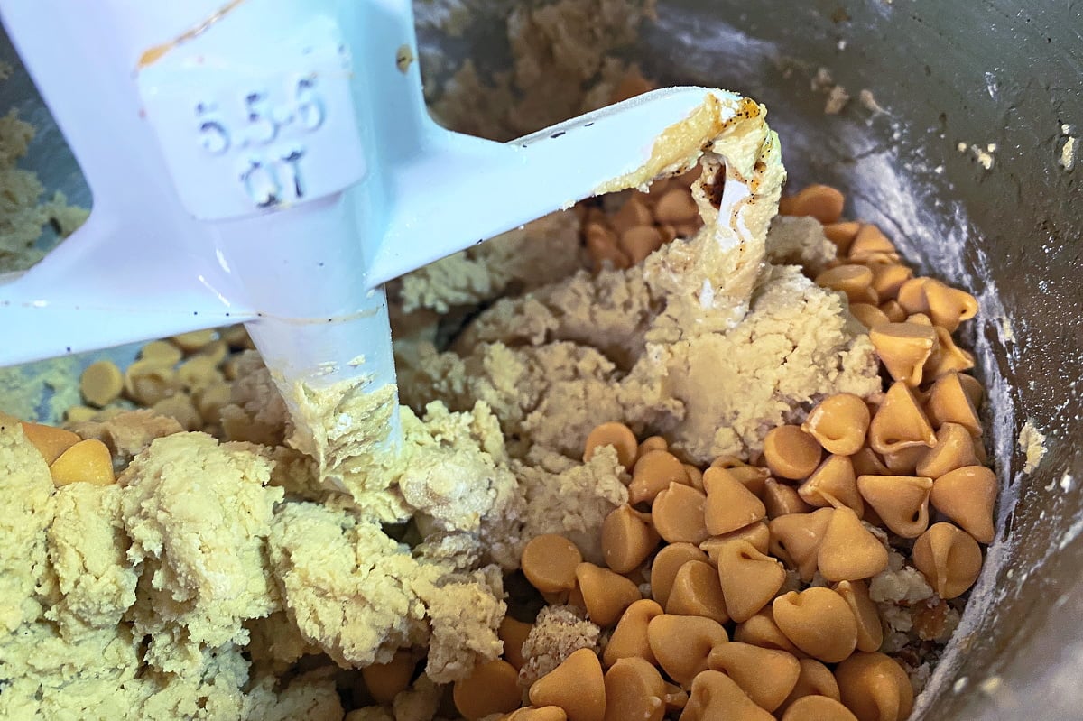 Cookie dough with butterscotch chips and pecans being mixed in a stand mixer