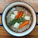 Dry navy beans and aromatics (rosemary, onions, carrots, and garlic) in a cast iron Dutch oven.