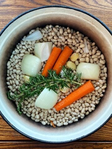 Dry navy beans and aromatics (rosemary, onions, carrots, and garlic) in a cast iron Dutch oven.