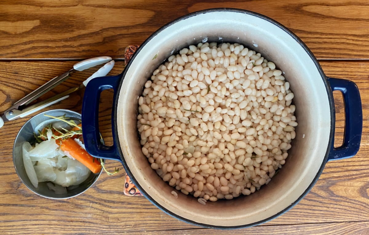 Navy beans in a cast iron Dutch oven, fully cooked and drained. Aromatics removed to the side.