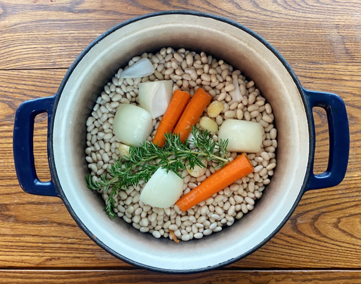 Dry navy beans and aromatics (rosemary, onions, carrots, and garlic) in a cast iron Dutch oven.