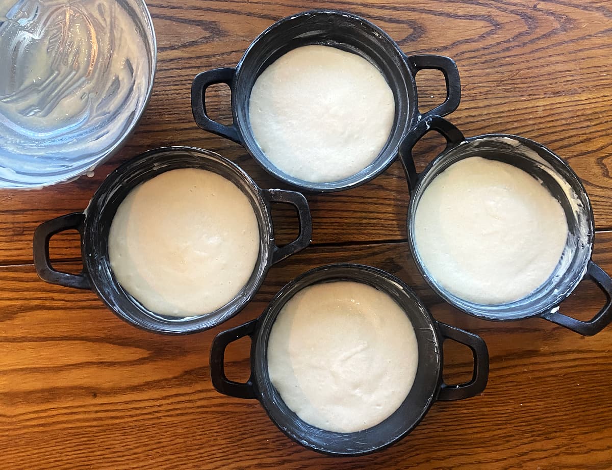 Pourable breakfast pizza dough spread into buttered mini cast iron skillets before baking.